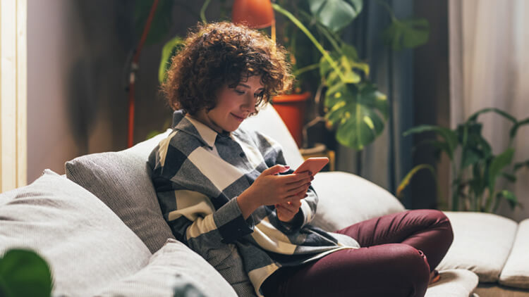 Woman sat on the sofa at home looking at her phone smiling