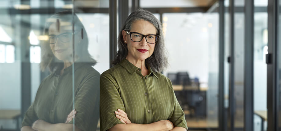 Female business woman wearing a green shirt stood ams folded in an office 