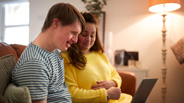 Young male adult with down syndrome using a laptop sat on the sofa at home