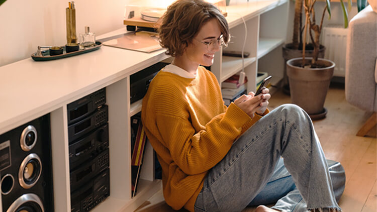 Young woman sat on the floor at home looking at her smart phone