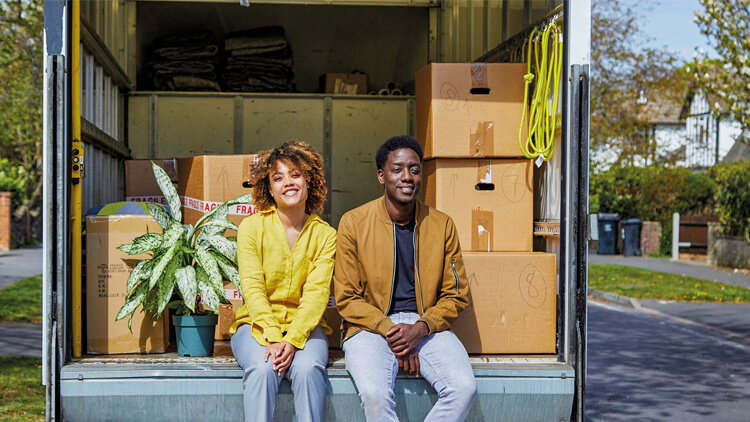 A couple moving home, sat on the back of a movers truck 